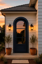House exterior with a dark blue door and two potted plants on either side at sunset.